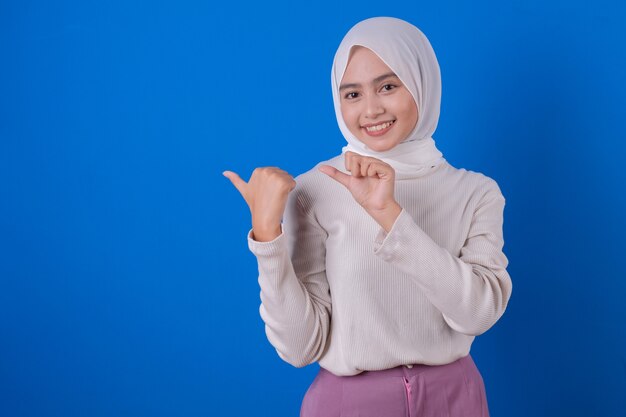 Bella donna asiatica allegra facendo uso dell'espressione di sorriso della maglietta bianca con il suo dito del pollice