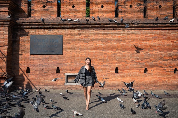 Bella donna asiatica brillantemente che cammina attraverso il gregge di piccioni che volano in Tha Phae gate, Chiang Mai, Thailand