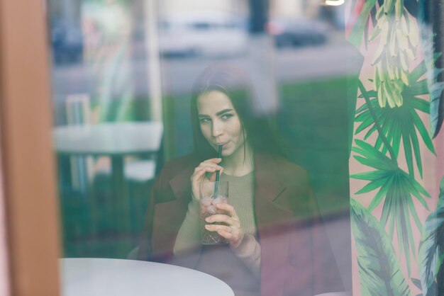 Bella donna asiatica che beve caffè al bar, sorride, parla al telefono