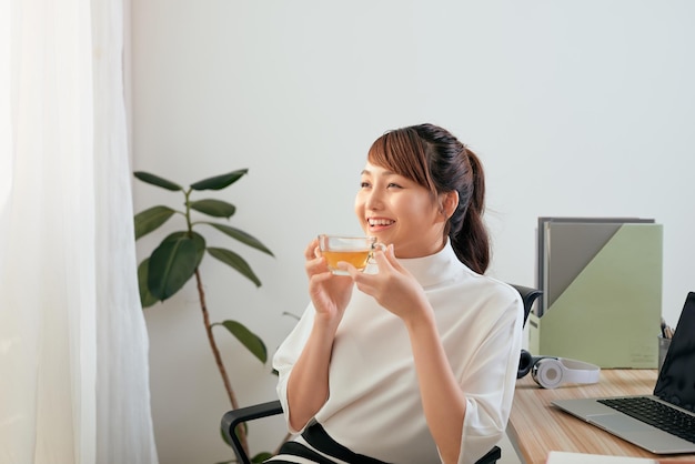 Bella donna asiatica che beve mentre è seduta nel suo ufficio