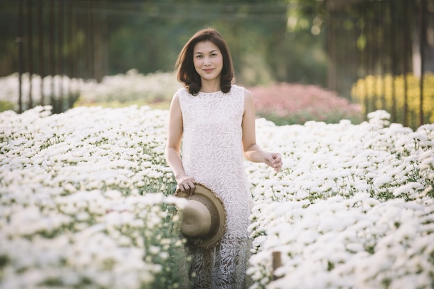 Bella donna asiatica che cammina e sorride in un giardino fiorito tropicale con modi felici con la calda luce del sole dallo sfondo