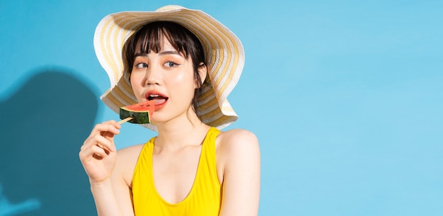 Bella donna asiatica che indossa tuta gialla sul blu e mangiare frutti tropicali