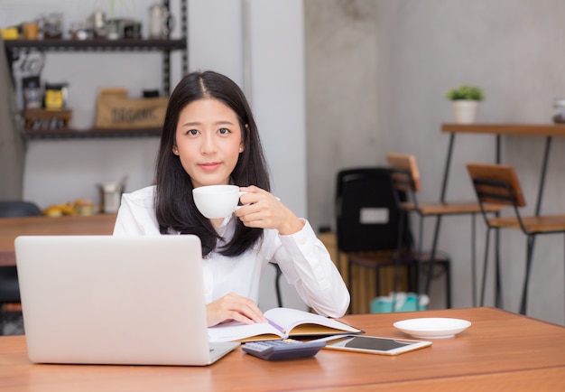 Bella donna asiatica che lavora online sul computer portatile e bere caffè.