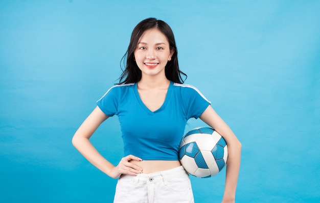 Bella donna asiatica che posa con il pallone da calcio sull'azzurro