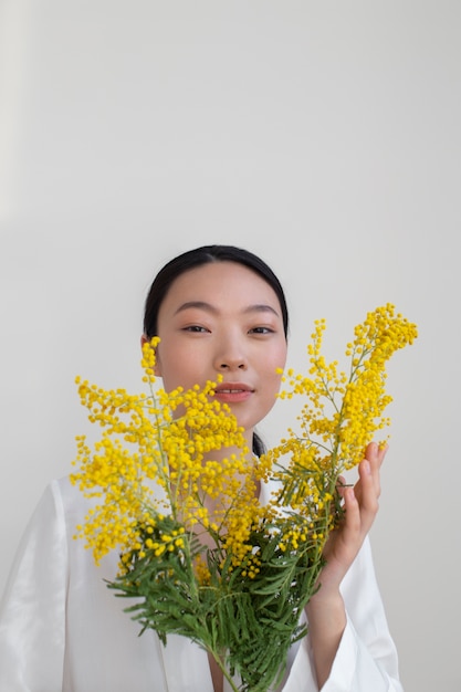 Bella donna asiatica che posa tenendo i fiori gialli con una pelle perfetta