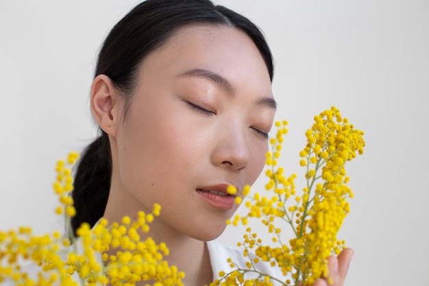 Bella donna asiatica che posa tenendo i fiori gialli con una pelle perfetta