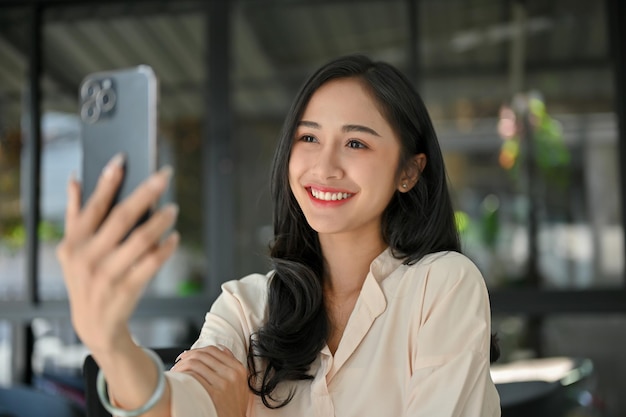 Bella donna asiatica che prende un selfie con il suo smartphone moderno mentre si rilassa al caffè