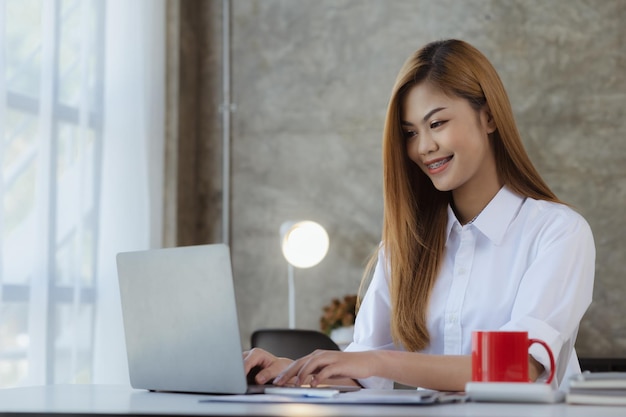 Bella donna asiatica che scrive con il suo laptop è un uomo d'affari giovane ed energico per gestire una società di avvio che conduce affari con la politica della nuova generazione