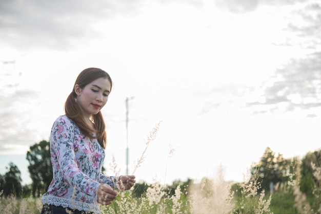 Bella donna asiatica che tiene fiore di erba nel campo la sera Gente della Thailandia