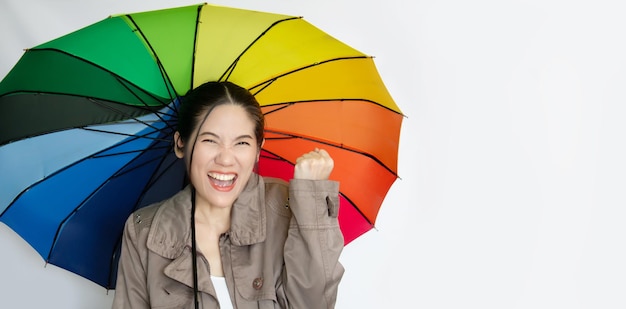 Bella donna asiatica che tiene un ombrello colorato alzando lo sguardo per vedere piovere e ridere con sentimento di vittoria e successo