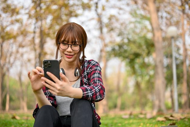 Bella donna asiatica che usa il suo telefono mentre si siede sull'erba rilassandosi nel parco