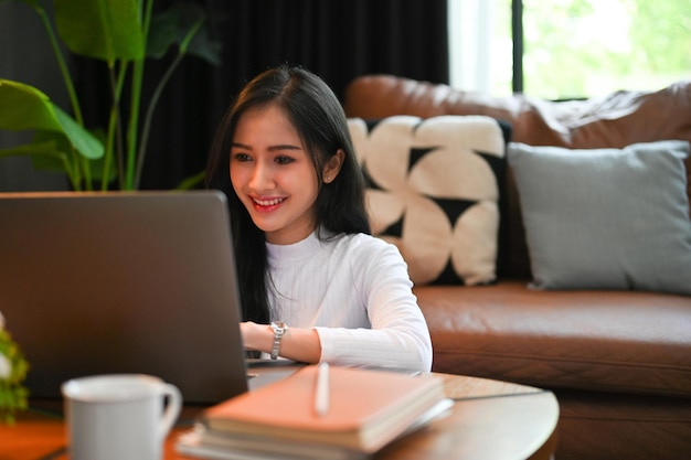 Bella donna asiatica che utilizza il laptop navigando in Internet lavorando al suo progetto da casa