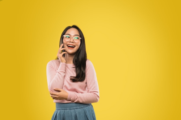 Bella donna asiatica con gli occhiali che sorride mentre chiama usando un telefono cellulare