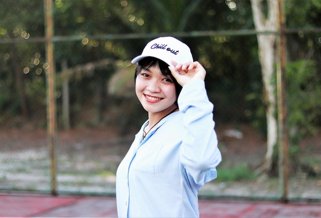 Bella donna asiatica con i capelli corti, indossa il cappello e sorride ampiamente sul campo da tennis