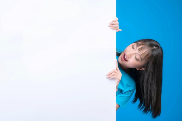 Bella donna asiatica con stile di capelli frangetta in maglietta blu sorridente e puntando il dito uno spazio vuoto per banner pubblicitario spazio vuoto copia bordo bianco un banner bianco isolato su sfondo blu