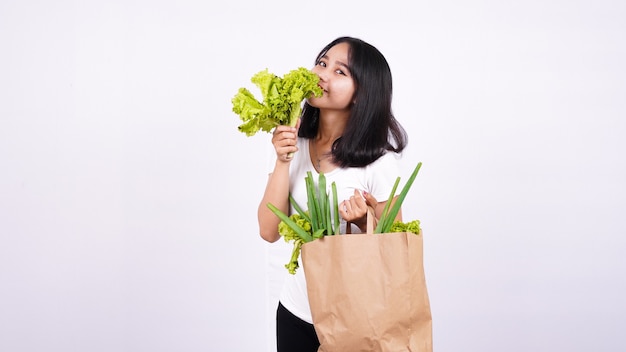 Bella donna asiatica con un sacchetto di carta di verdure fresche e tenendo la lattuga fresca con superficie bianca isolata