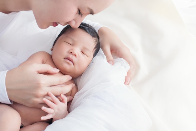 Bella donna asiatica felice che esamina il suo bambino addormentato sul letto bianco