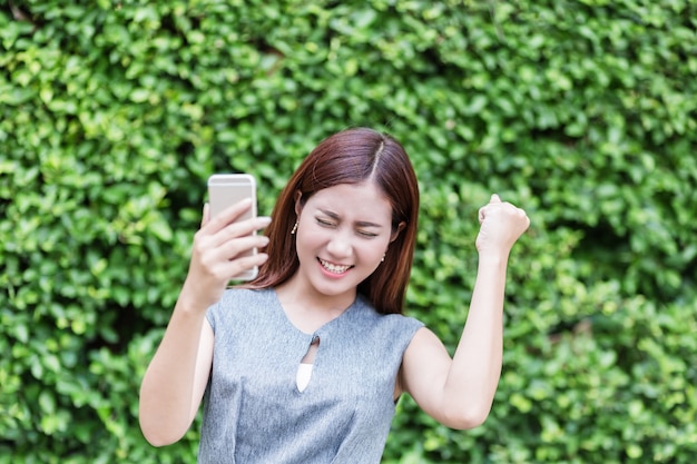 bella donna asiatica felice con lo smartphone in giardino