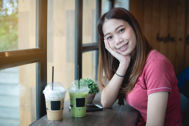 Bella donna asiatica in caffetteria, guardando la fotocamera, con cappuccino ghiacciato e tè verde matcha