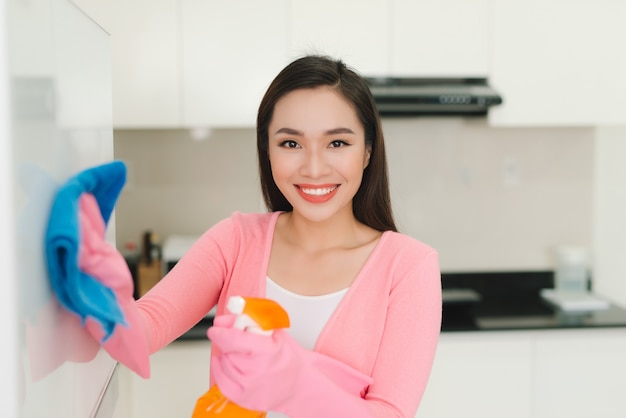 Bella donna asiatica in guanti protettivi che pulisce l'armadio da cucina