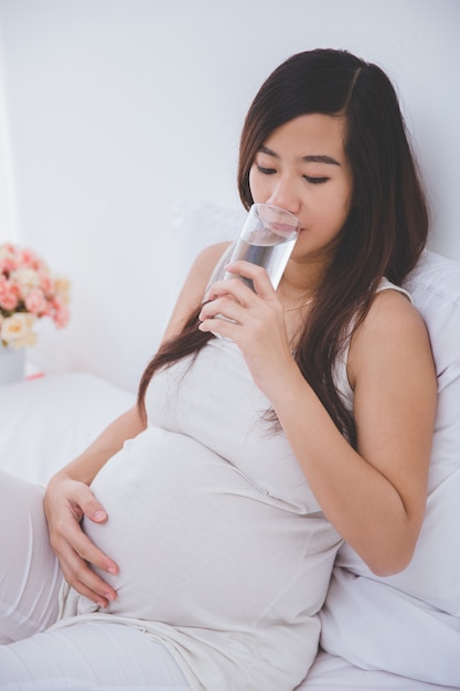 Bella donna asiatica incinta che tiene un bicchiere d'acqua