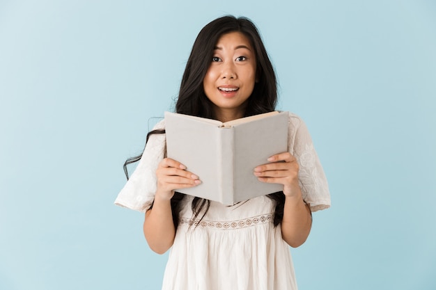Bella donna asiatica isolata sopra il libro di lettura della parete blu