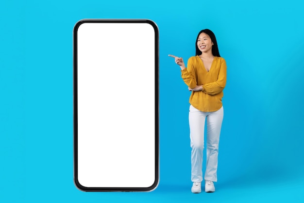 Bella donna asiatica magra che punta a un enorme smartphone