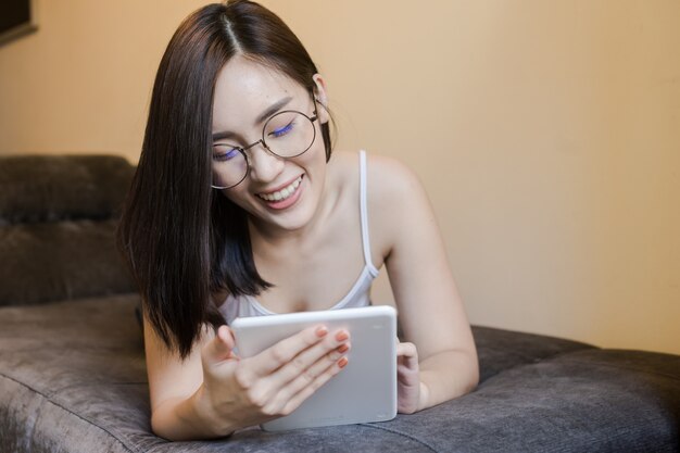 Bella donna asiatica utilizzando smart phone sul letto. la signora usa taplet per lo shopping online