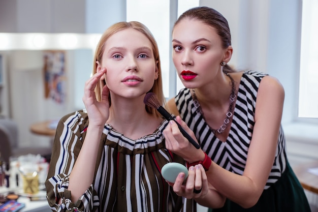 Bella donna attraente che guarda il suo viso mentre è nel salone di bellezza