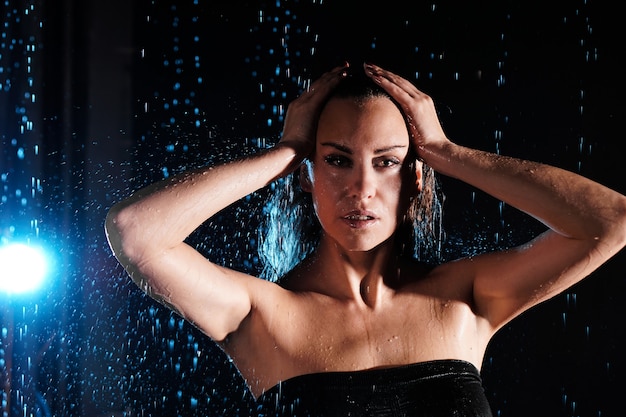 Bella donna bagnata sotto le gocce di pioggia che cadono - foto in studio con luce blu