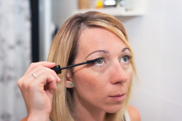 Bella donna bionda che applica mascara sui suoi cigli