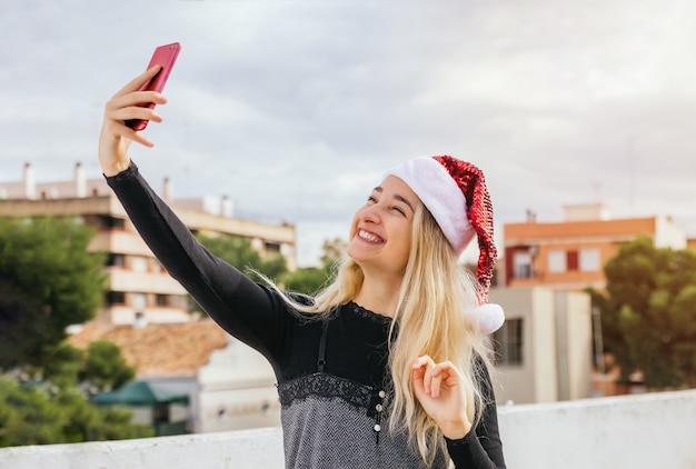 Bella donna bionda che cattura un selfie con il cellulare per il giorno di Natale.