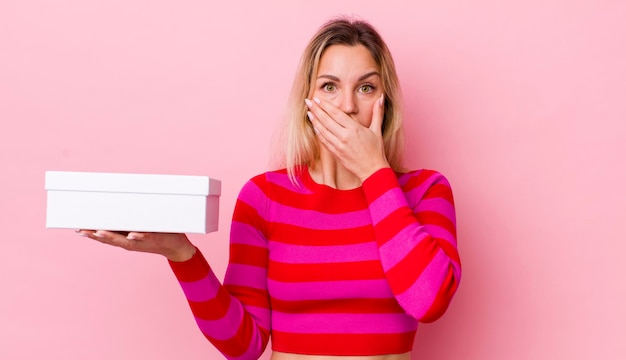 Bella donna bionda che copre la bocca con le mani con un concetto di scatola bianca scioccata