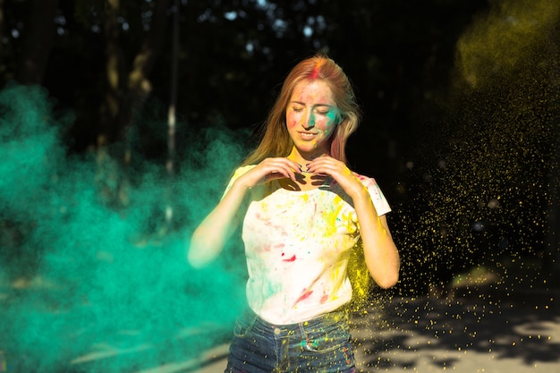 Bella donna bionda che gioca con la vernice secca gialla e verde Holi nel parco