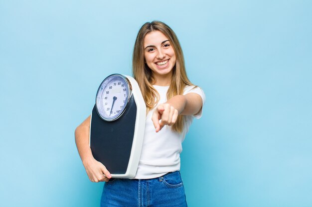 Bella donna bionda che punta in avanti con un sorriso soddisfatto, fiducioso, amichevole, scegliendo te