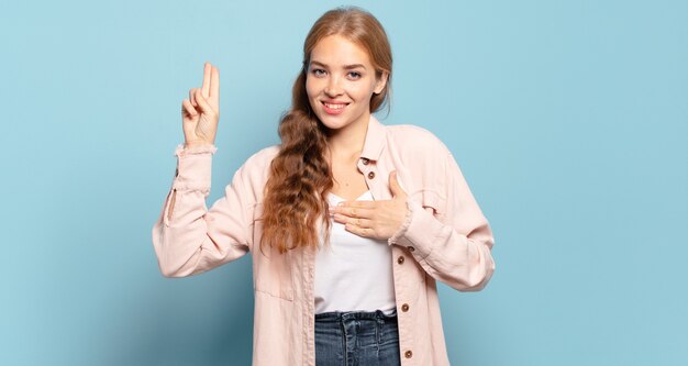 Bella donna bionda che sembra felice, sicura e degna di fiducia, sorridente e che mostra il segno della vittoria, con un atteggiamento positivo