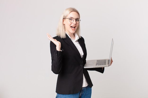 Bella donna bionda che si sente felice e stupita da qualcosa di incredibile e tiene in mano un laptop