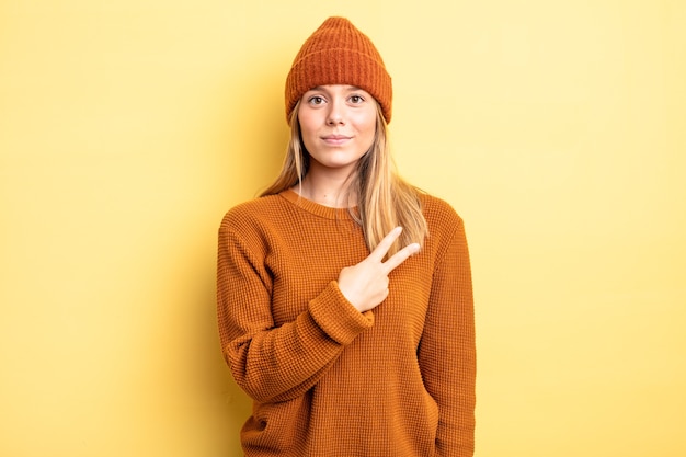 Bella donna bionda che si sente felice, positiva e di successo, con la mano che fa la forma a v sul petto, mostrando vittoria o pace