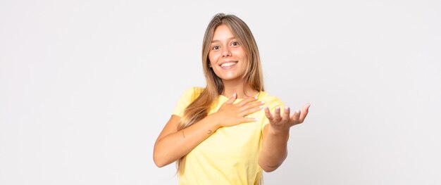 Bella donna bionda che si sente innamorata e sembra carina, adorabile e felice, sorride romanticamente con le mani accanto al viso