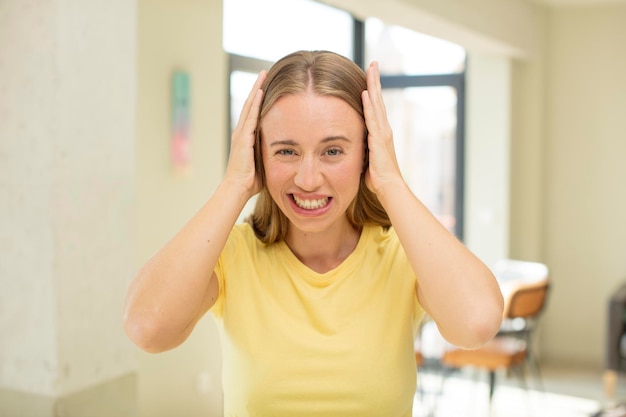 bella donna bionda che si sente stressata, preoccupata, ansiosa o spaventata, con le mani sulla testa, in preda al panico per errore