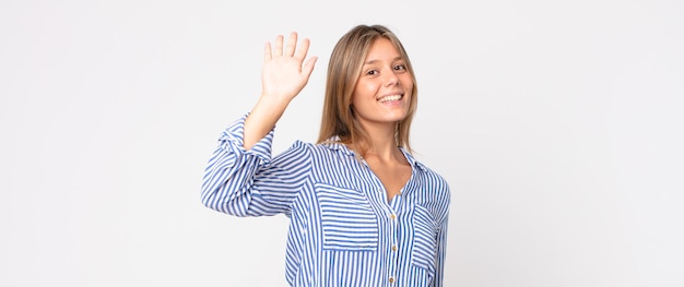 Bella donna bionda che sorride allegramente e indica la telecamera mentre fa una chiamata dopo un gesto, parlando al telefono