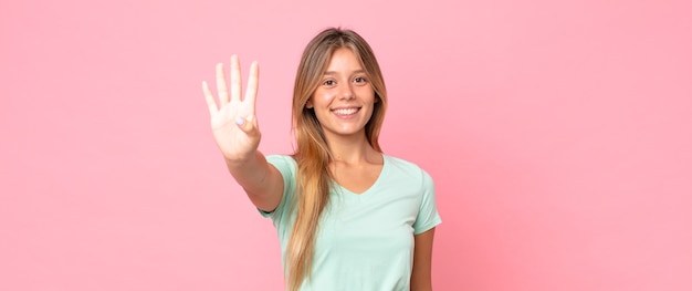 Bella donna bionda che sorride e sembra amichevole, mostra il numero quattro o il quarto con la mano in avanti, conto alla rovescia