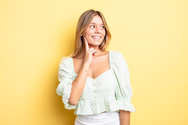 Bella donna bionda che sorride felice e sogna ad occhi aperti o dubita, guardando di lato