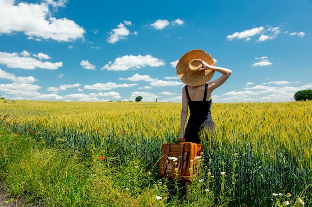 Bella donna bionda con la valigia in strada di campagna vicino al campo di grano