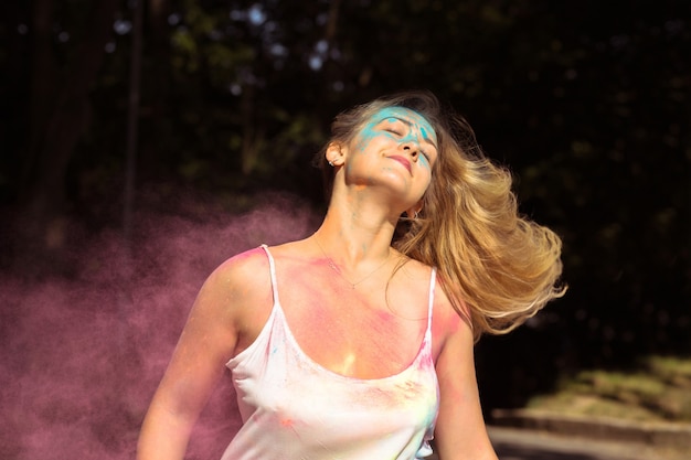 Bella donna bionda con lunghi capelli ricci che svolazzano al vento con vernice secca Holi