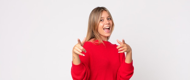 Bella donna bionda con un cattivo atteggiamento che sembra orgogliosa e aggressiva, che punta verso l'alto o fa un segno divertente con le mani