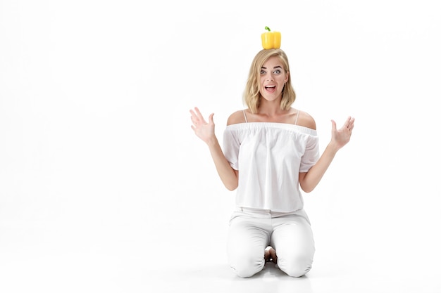 Bella donna bionda divertente in una camicetta bianca che tiene peperone dolce giallo. Dieta sana e dieta