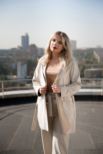 Bella donna bionda in cappotto beige in piedi sul tetto della casa.