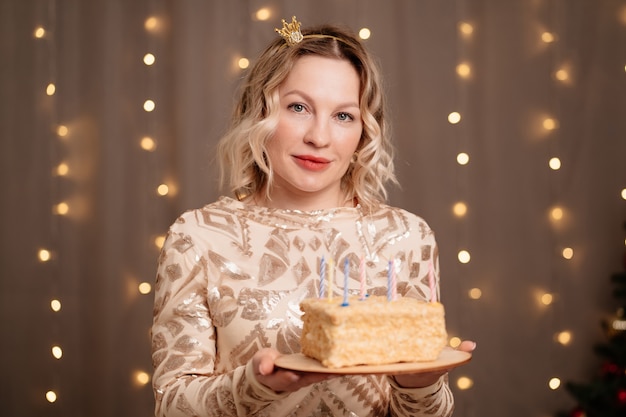 Bella donna bionda in una piccola corona in testa con una torta di compleanno e candele.