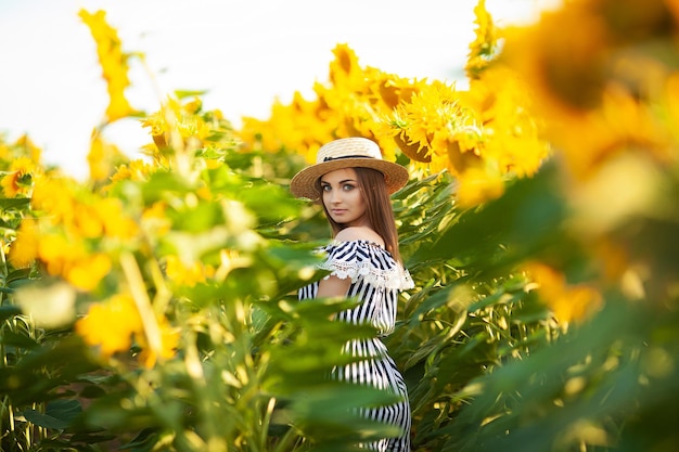 Bella donna bionda nel campo di fiori al tramonto in cappello di paglia